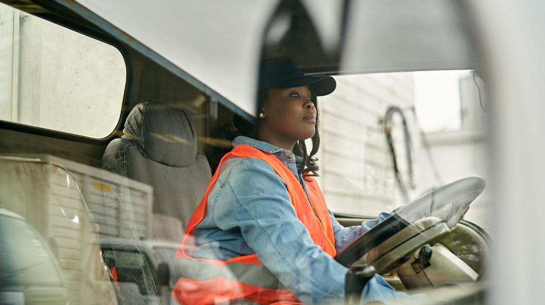 Woman truck driver sitting in a truck while holding on the steering wheel.