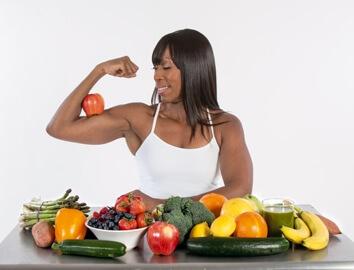 Woman flexing muscles around fruits and vegetables